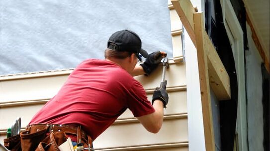Contractor fastening a new vinyl siding panel to a house
